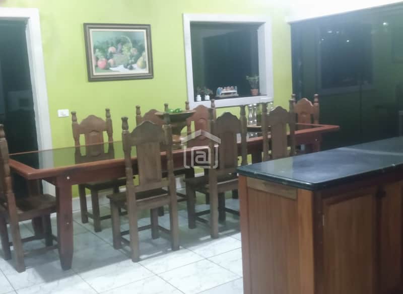 Sala de jantar ampla com mesa de madeira e tampo de vidro, cadeiras rústicas e balcão com pia. Decoração clean.