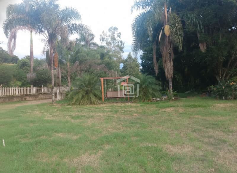 Área externa com gramado, balanço de madeira e palmeiras. Paisagem natural e cerca branca ao fundo.