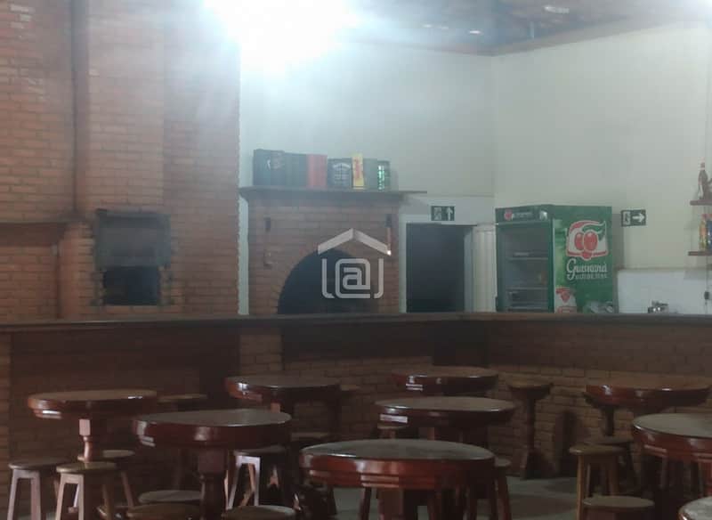 Bar aconchegante com mesas de madeira, balcão rústico em tijolo e refrigerador de bebidas.