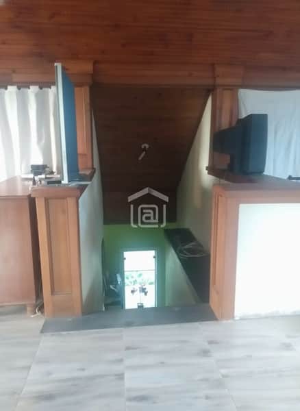 Sala com piso claro e vista para escada de madeira, com TV antiga e iluminação natural.