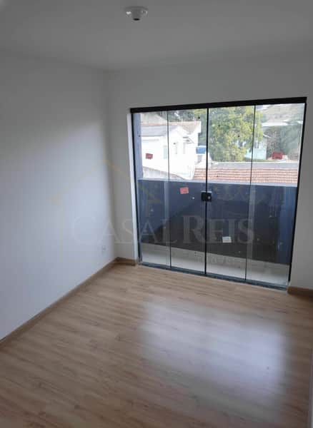 Quarto claro com piso amadeirado e sacada envidraçada com vista externa.