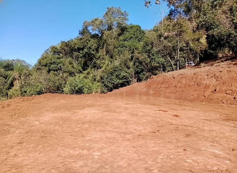 Terreno plano de terra batida em área externa com vegetação ao fundo sob céu azul.