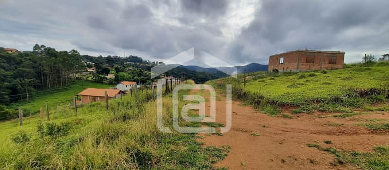 Terreno em declive com construção de tijolos à vista e vegetação. Céu nublado ao fundo.