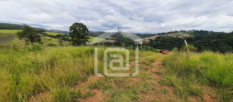 Terreno gramado com vista para montanhas e céu nublado. Carro laranja ao fundo. Natureza exuberante.
