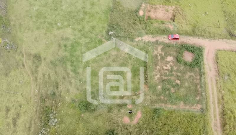Terreno rural com pasto, cerca e estrada de terra. Carro vermelho visível. Vista aérea.
