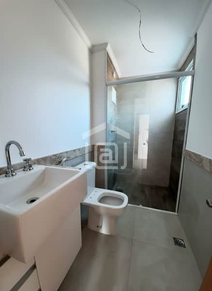 Banheiro claro com pia moderna, vaso sanitário e box de vidro. Detalhes em mármore e piso cerâmico.