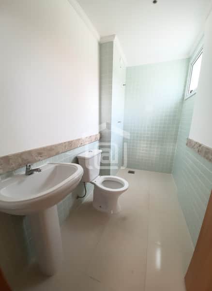 Banheiro claro com pia de coluna, vaso sanitário e revestimento em azulejo verde claro. Ambiente iluminado e clean.