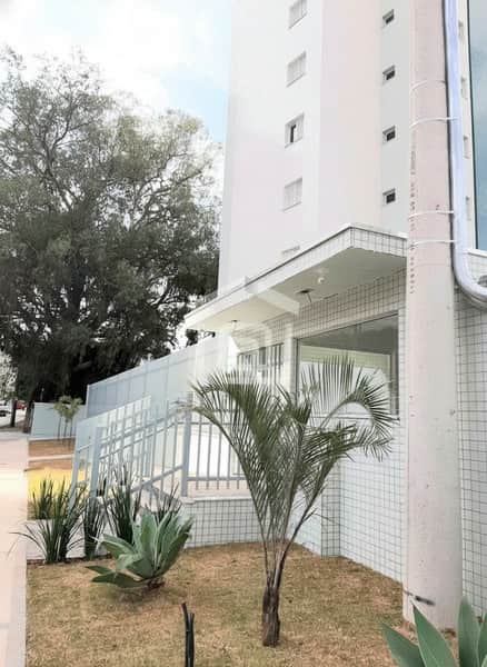 Fachada de prédio branco com guarita, paisagismo e rampa de acesso. Detalhes em cerâmica clara.