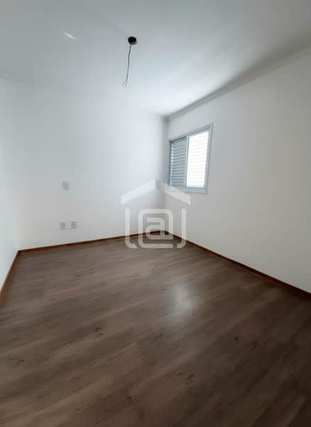 Quarto vazio com piso amadeirado, paredes brancas e janela com persiana. Ambiente claro e arejado.