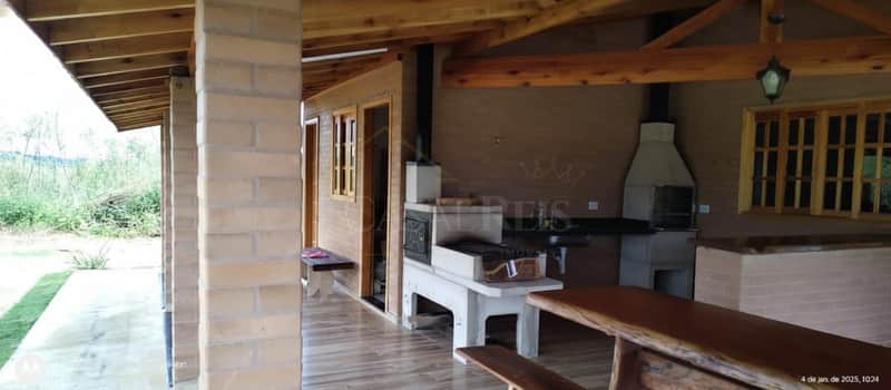 Área externa com churrasqueira e forno a lenha. Bancada rústica de madeira e piso cerâmico.