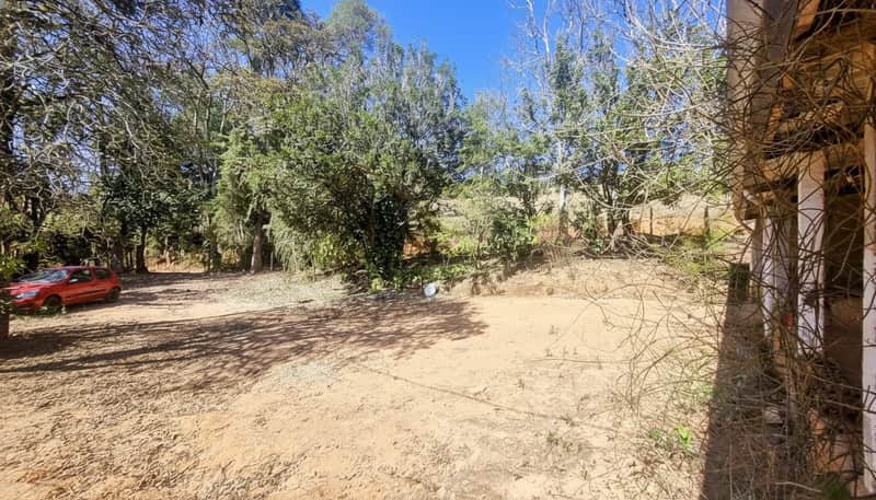 Área externa ensolarada com vegetação, carro vermelho e construção rústica com colunas.