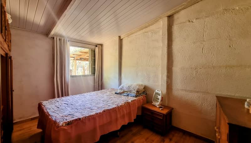 Quarto simples com cama de solteiro, paredes rústicas e piso de madeira. Ambiente aconchegante e iluminado.