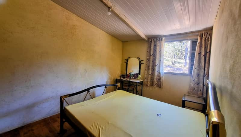 Quarto simples com cama de metal, paredes texturizadas e janela com cortinas estampadas. Decoração vintage.
