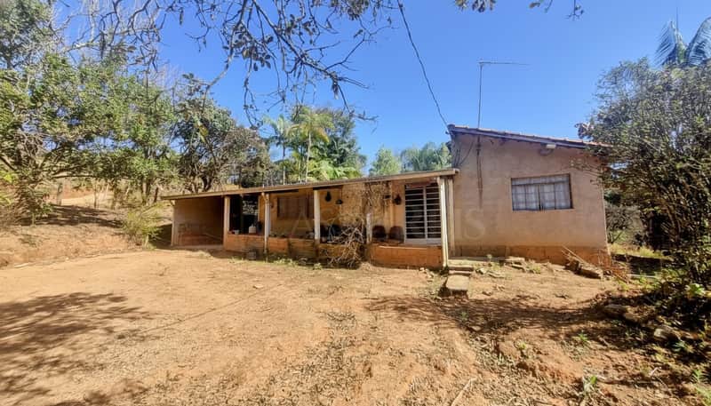 Casa térrea com varanda e fachada rústica em área externa ensolarada e arborizada.