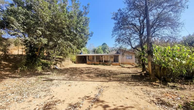 Casa térrea com varanda em área externa ampla e ensolarada, cercada por árvores.