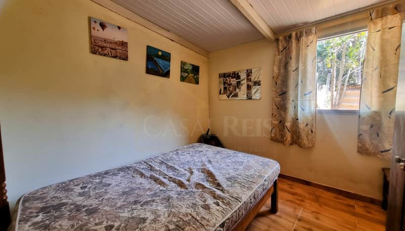 Quarto simples com cama de solteiro, quadros na parede e janela com cortinas estampadas.