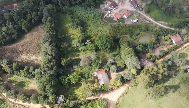 Vista aérea de imóvel rural com vegetação exuberante, casa com telhado aparente e estradas de terra.