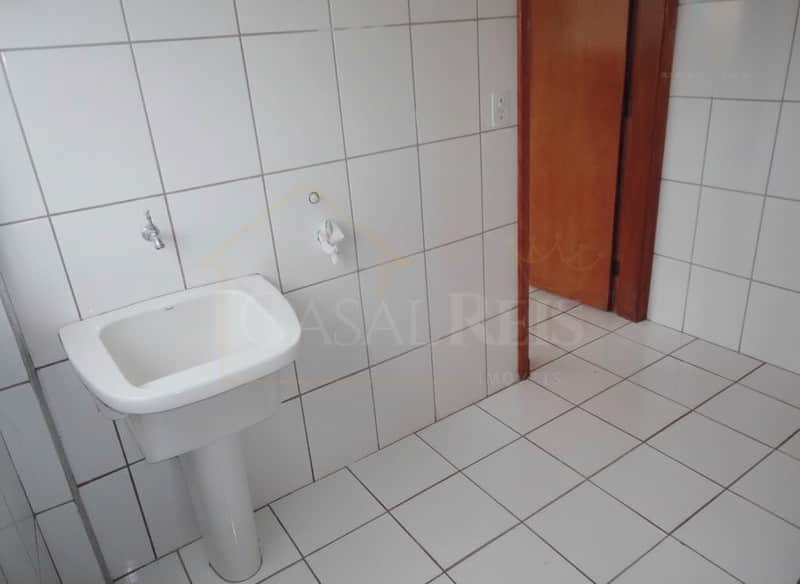 Banheiro com pia branca, azulejos claros e porta de madeira. Ambiente clean e funcional.