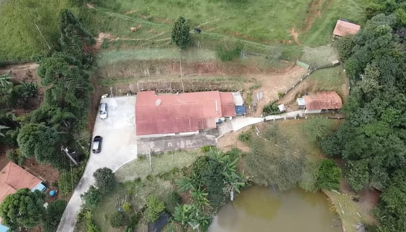 Vista aérea de propriedade rural. Casa com telhado vermelho, lagoa, pasto e árvores.