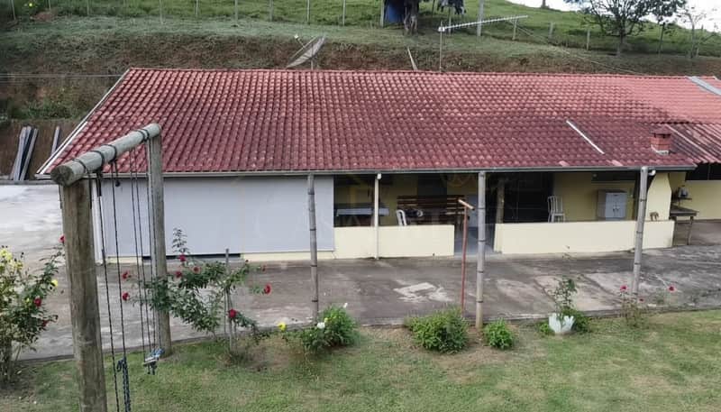 Área externa com casa térrea e telhado rústico. Balanço de madeira e jardim florido em primeiro plano.