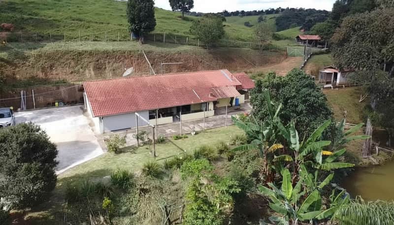 Casa de campo com telhado vermelho, área externa com gramado e lago. Paisagem verde e tranquila.