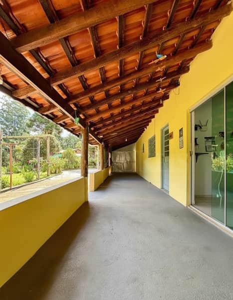 Varanda externa ampla com piso cinza, paredes amarelas e telhado rústico de madeira e telhas.