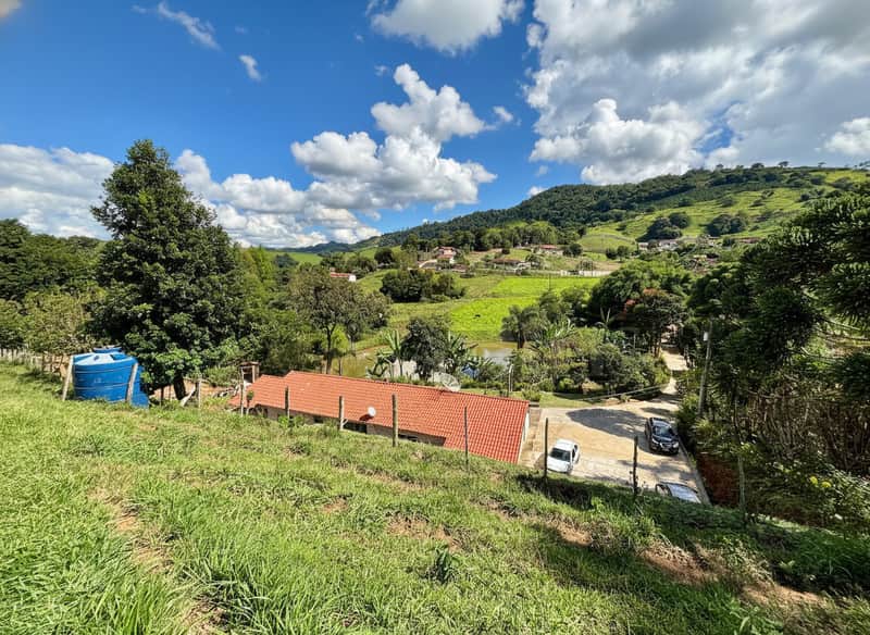 Área externa ensolarada com casa de telhado vermelho, gramado verde e céu azul com nuvens.