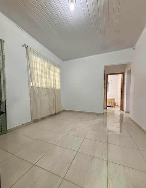 Sala ampla e iluminada com piso cerâmico claro, cortina bege e teto branco de madeira.
