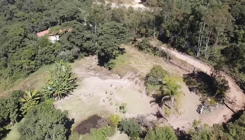Área externa com lago, vegetação exuberante e casa ao fundo. Vista aérea da propriedade rural.