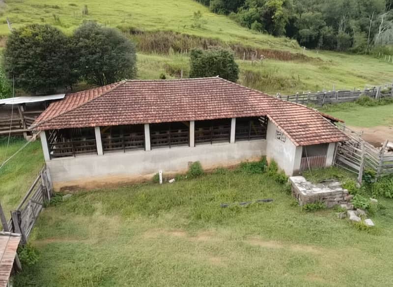 Construção rural com varanda e telhado rústico em área verde. Detalhes em madeira e alvenaria.