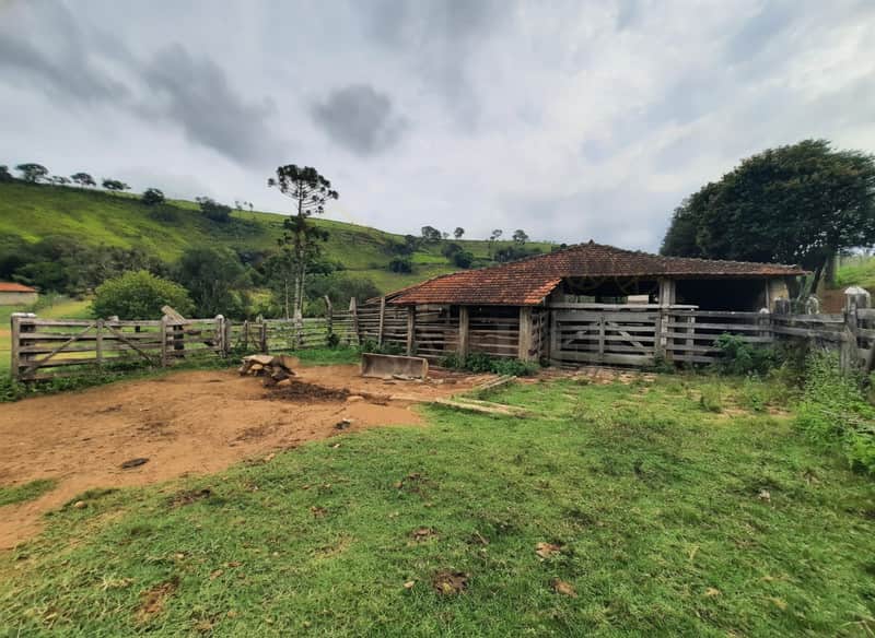 Área externa com curral de madeira rústica e pasto verde em dia nublado.