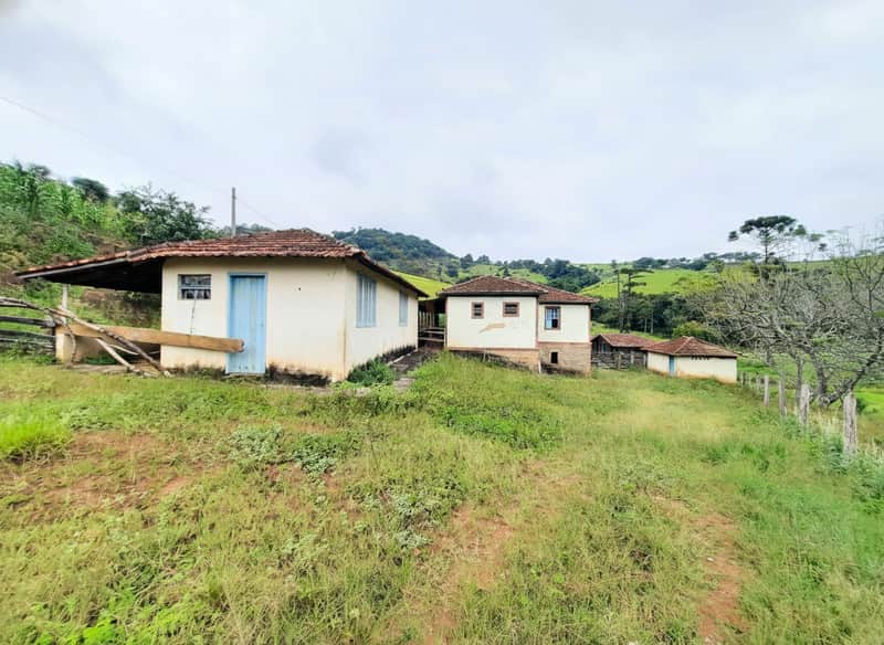 Fachada de casas rurais antigas em área verde, com grama alta e céu nublado.