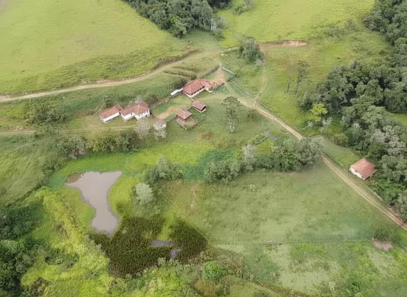 Vista aérea de fazenda com casa, pasto, lago e vegetação exuberante.