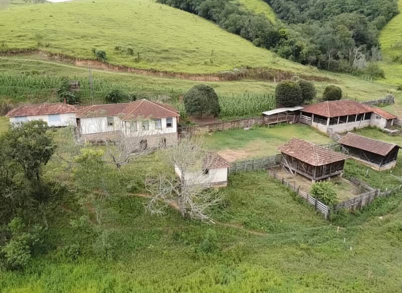 Fazenda com casa antiga e currais. Vista panorâmica da área externa rural com pasto e vegetação.