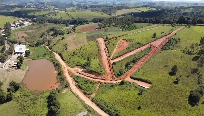 Terreno em área rural com lago, vegetação e estradas de terra vermelha. Vista aérea.