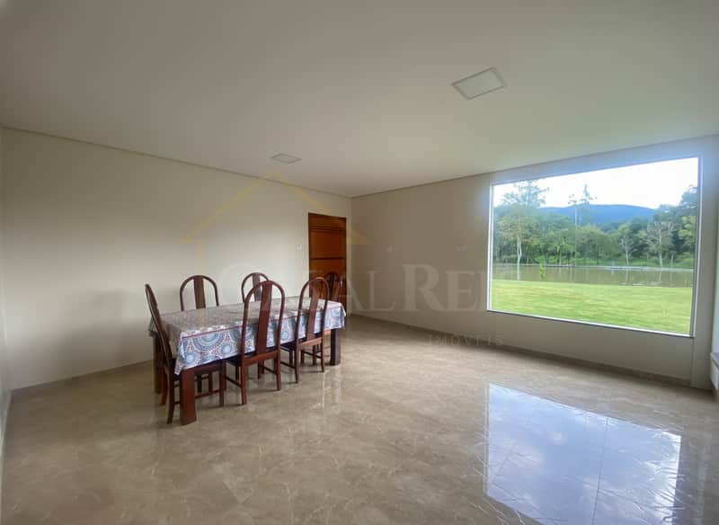 Sala ampla com mesa e vista para área externa com lago e montanhas. Piso brilhante.
