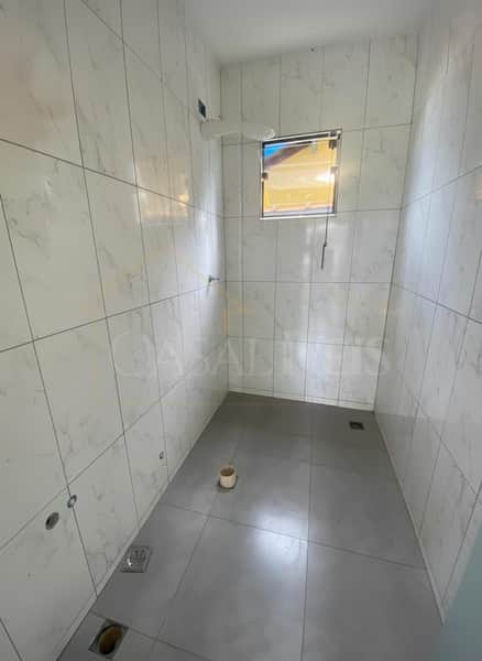 Banheiro com revestimento marmorizado claro, piso cinza e janela. Ambiente clean e iluminado.