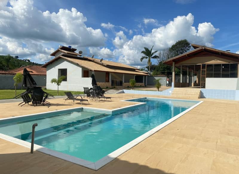 Área externa com piscina, espreguiçadeiras e casas ao fundo em dia ensolarado. Lazer e conforto.