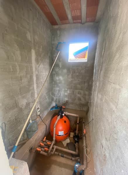 Casa em construção. Pequena área com filtro de piscina laranja e paredes de cimento.