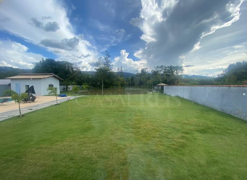 Ampla área externa com gramado, lago e construção. Céu azul com nuvens.