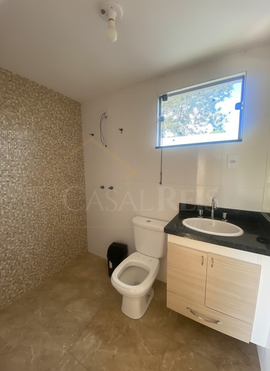 Banheiro claro com pia de granito preto, vaso sanitário branco e parede com mosaicos bege. Janela basculante.