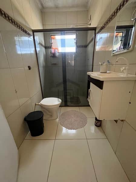 Banheiro claro com box, pia com armário, vaso sanitário e tapete redondo no piso de cerâmica.
