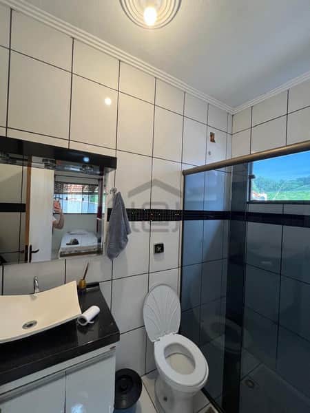 Banheiro com pia moderna, vaso sanitário branco e box com azulejos pretos. Decoração clean e funcional.