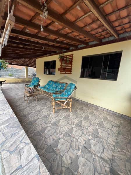 Área externa coberta com piso rústico e mobiliário de bambu. Paredes claras e janelas escuras.