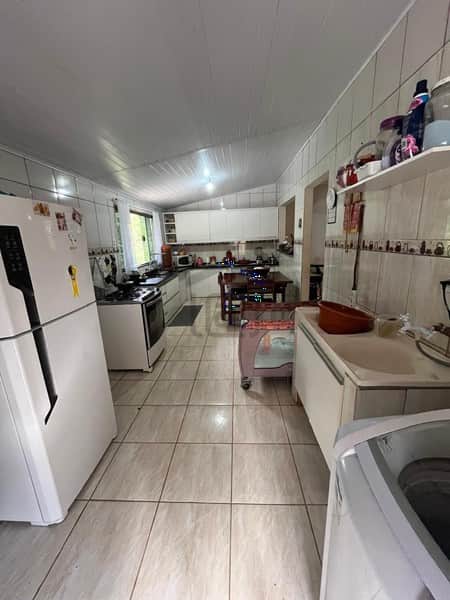 Cozinha ampla com piso cerâmico, armários brancos, geladeira e mesa de jantar ao fundo.