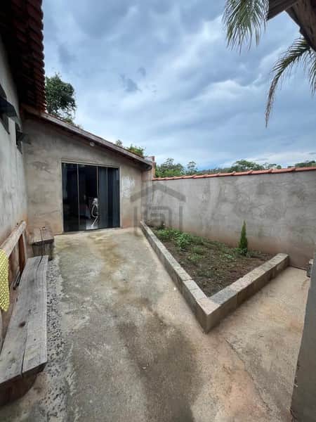 Área externa com banco rústico, jardim triangular e parede de concreto sob céu nublado.