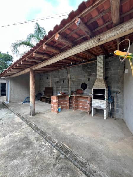 Área externa com churrasqueira de tijolos e alvenaria. Telhado rústico com vigas de madeira aparente. Piso de concreto.