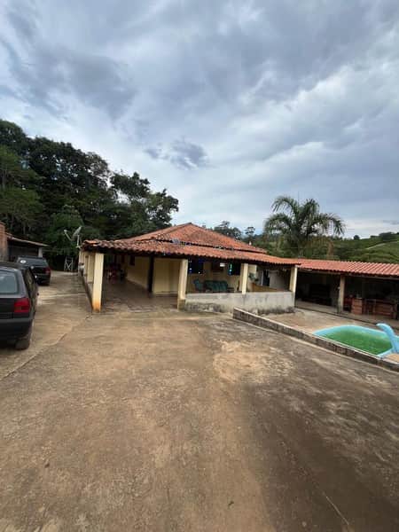 Casa com área externa ampla, piscina e varanda. Arquitetura rústica, céu nublado.