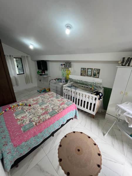Quarto infantil espaçoso com cama, berço branco, tapete redondo e armário. Ambiente claro e organizado.
