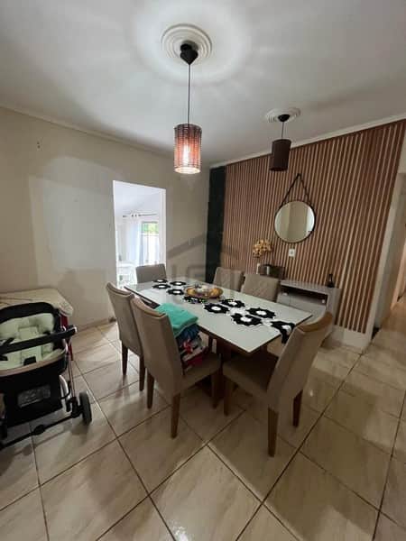 Sala de jantar clean com mesa, cadeiras bege e luminárias pendentes. Destaque para parede com painel ripado.